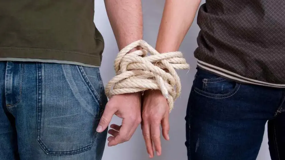 Duas pessoas com as mãos amarradas por uma corda