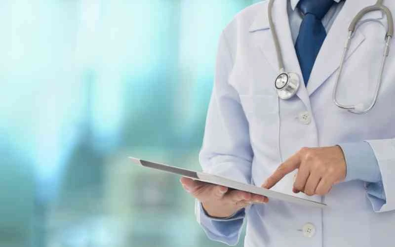 Médico de jaleco e estetoscópio segurando um tablet