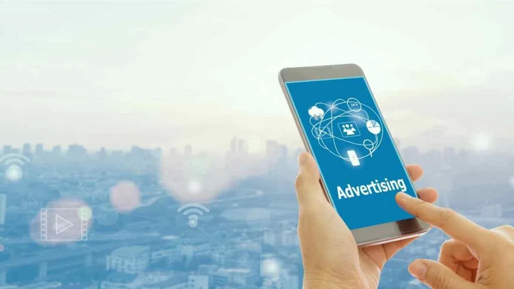 Mão apontando para um celular com ícones de publicidade na tela