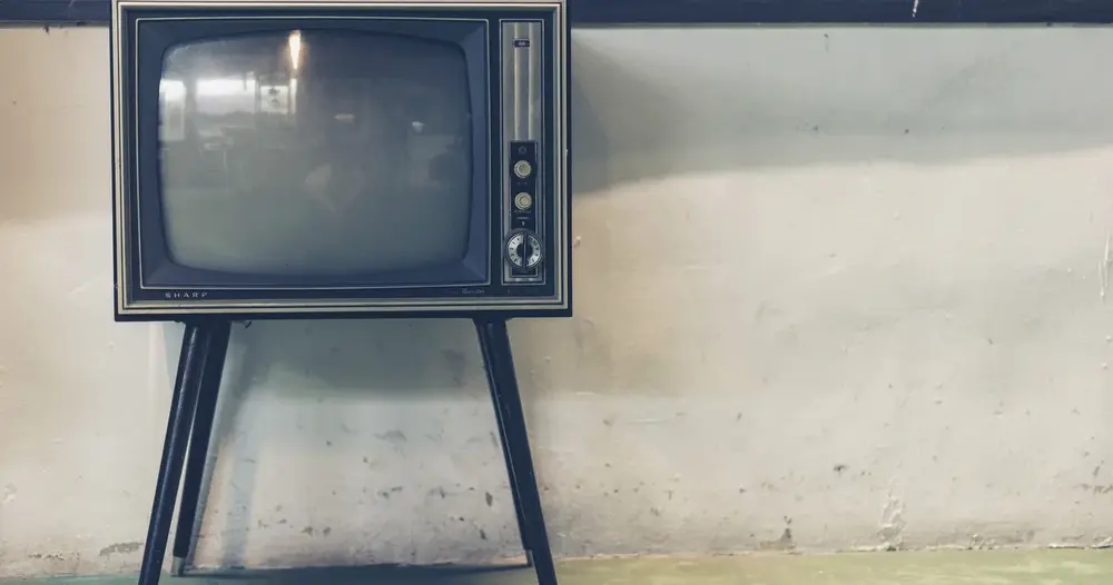 Televisão antiga de tubo sobre pés de metal diante de parede clara