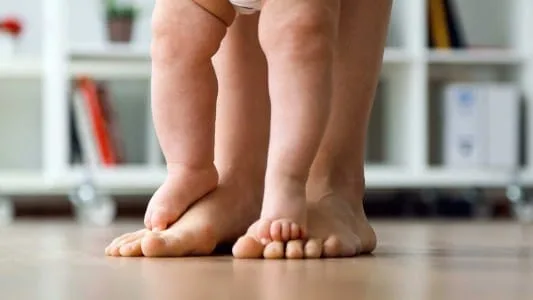 Pés descalços de uma criança e de um bebê sobre o piso de madeira